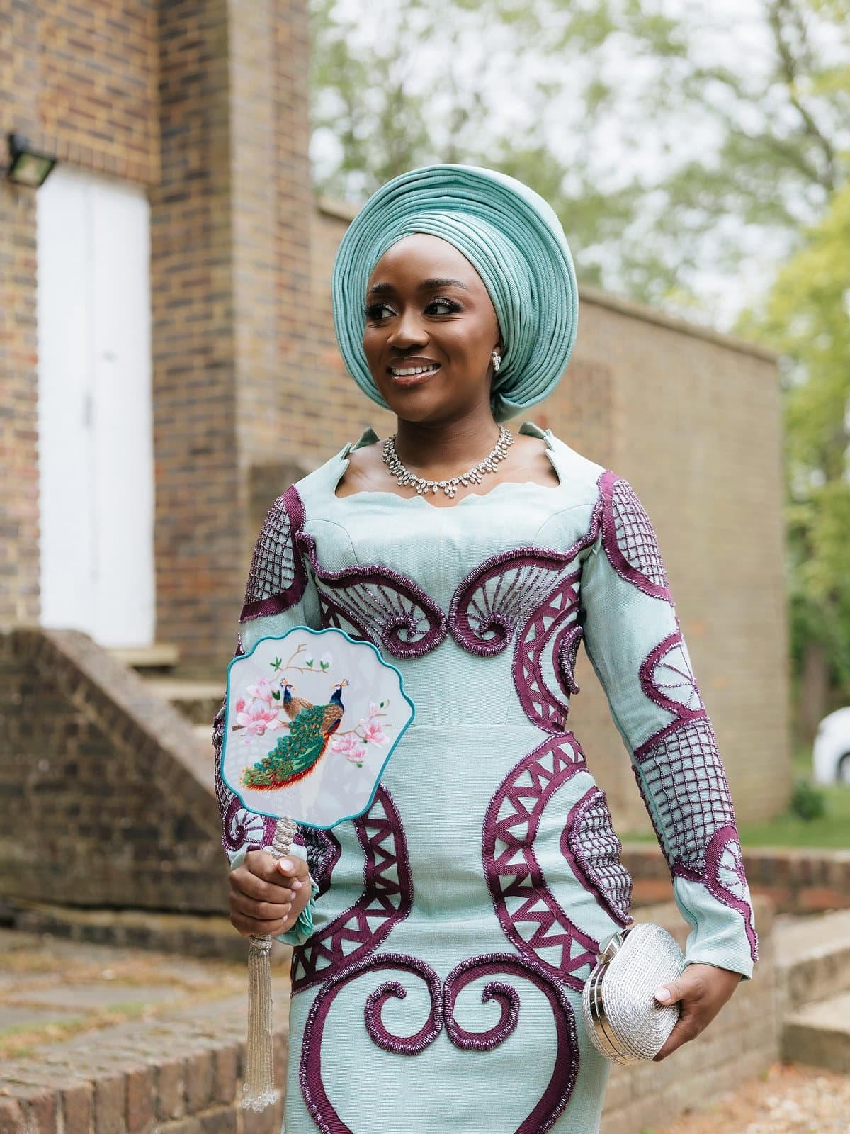 A hand-painted fan and a mint-and-maroon aso-ebi, caught mid-laugh.
