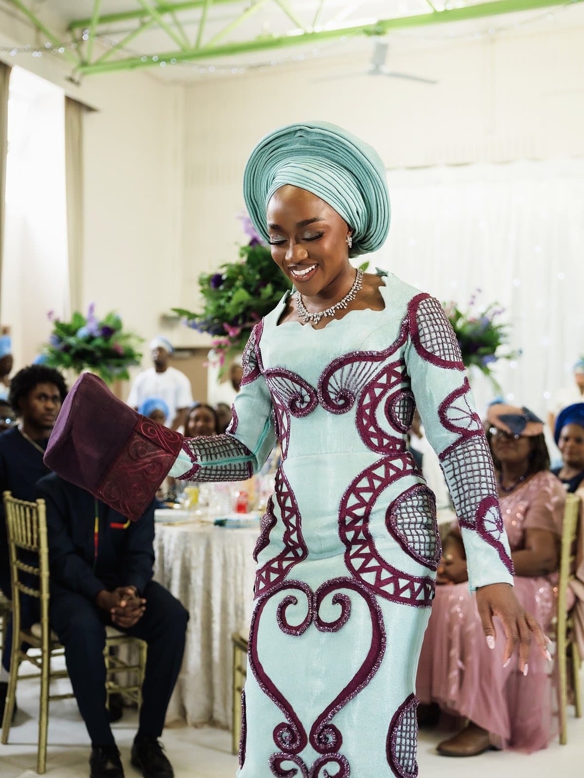 Same aso-ebi, a different room, a gift extended across a reception table.